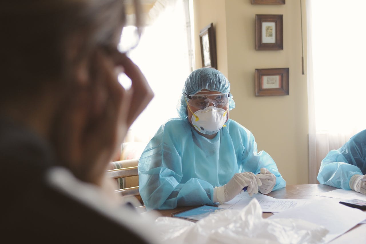 A healthcare worker in full protective gear conducts a consultation indoors, emphasizing safety during a health crisis.