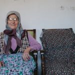 الرئيسة Elderly woman sitting in a traditional Turkish home, showcasing cultural attire and interior decor.