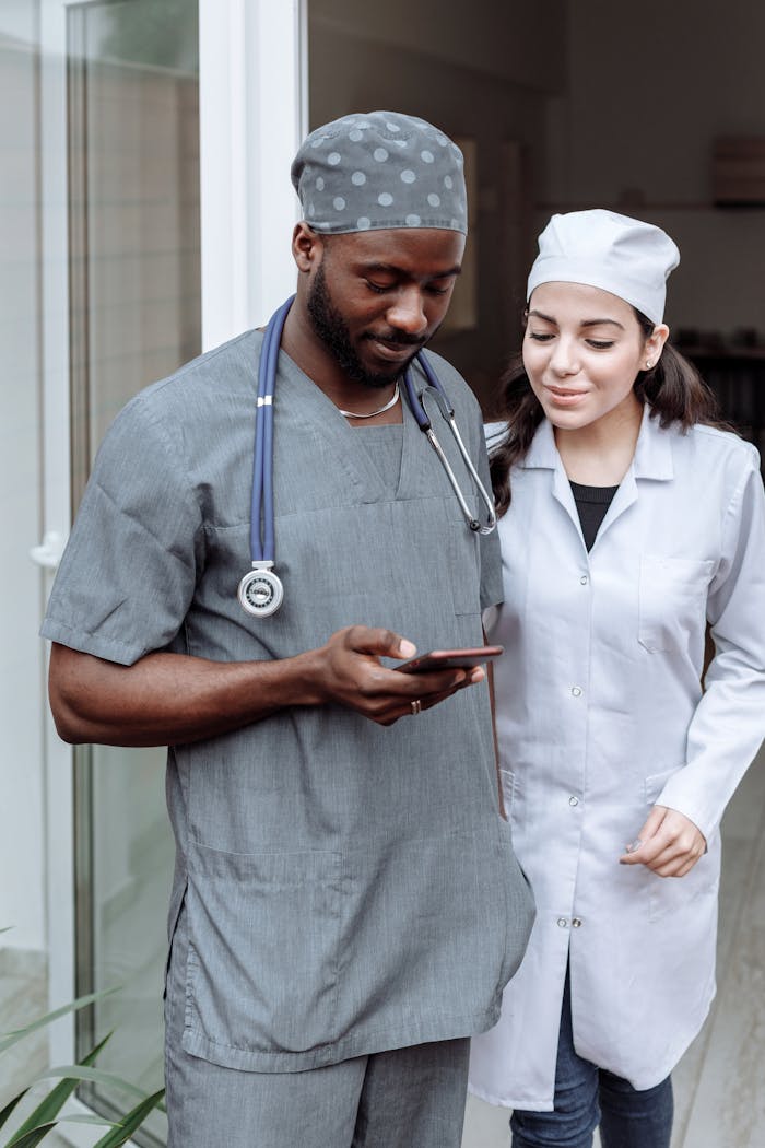 Two healthcare professionals in scrubs discussing patient care via smartphone.