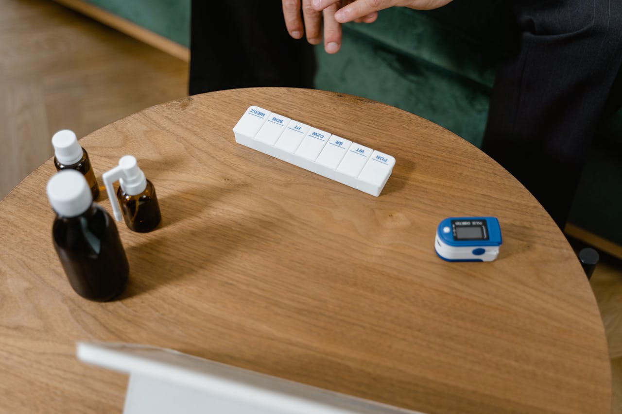 Pill organizer and medication bottles on a wooden table with a pulse oximeter.