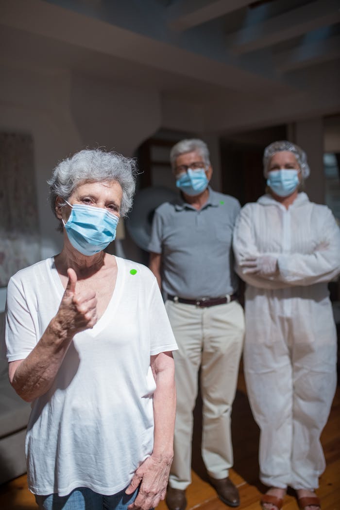 Senior woman thumbs up with healthcare staff in masks for home care